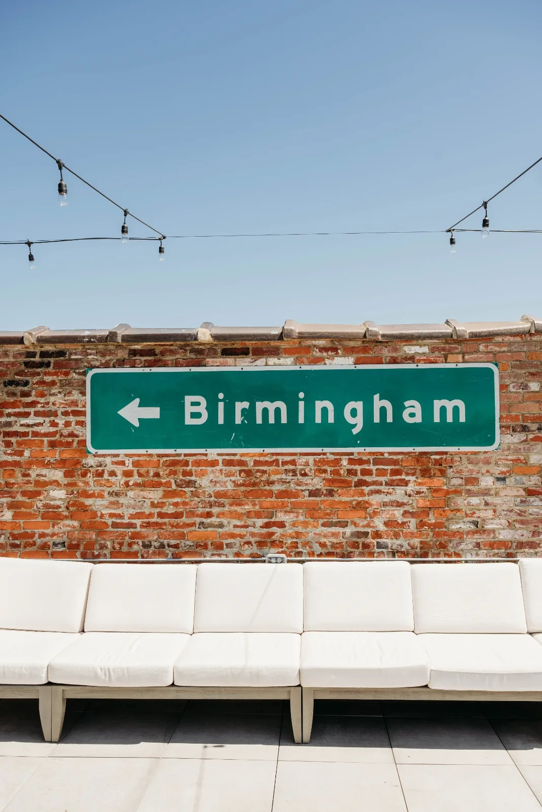 A green Birmingham highway sign mounted on a brick rooftop patio wall
