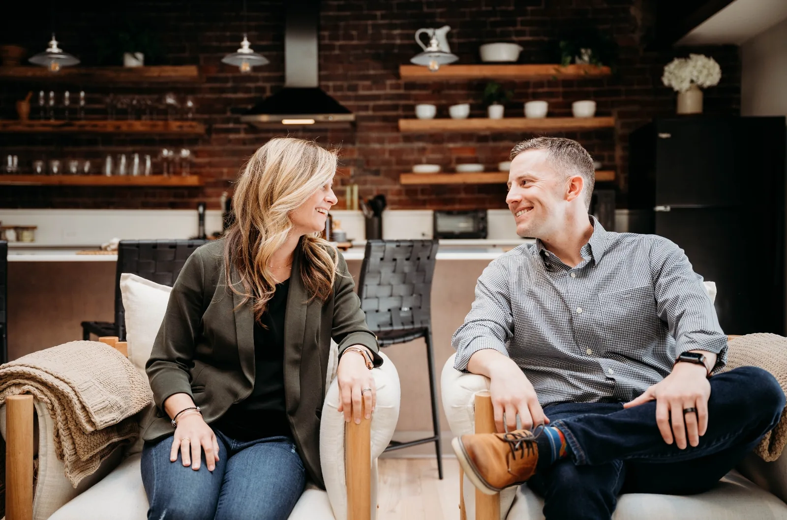 Jeff and Chelsea seated in armchairs in front of an exposed brick wall