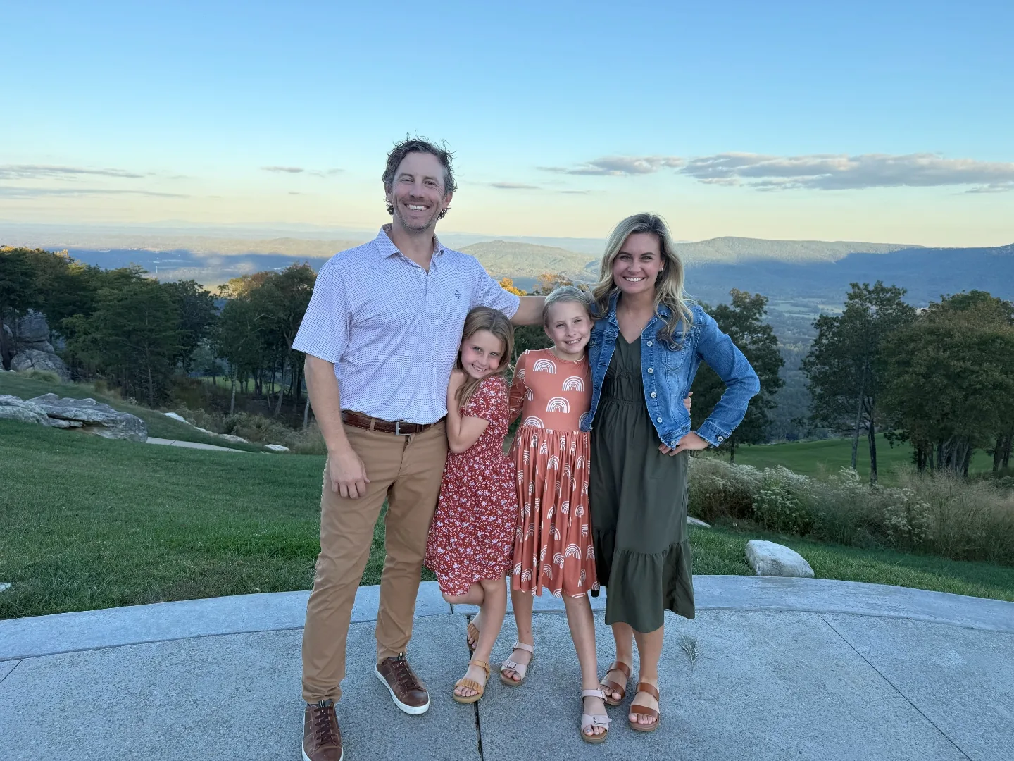 Jeff, Chelsea and two of their daughters standing on a stone terrace on the brow at McLemore at golden hour, the Lookout Mountain ridgeline and valley stretching out behind them