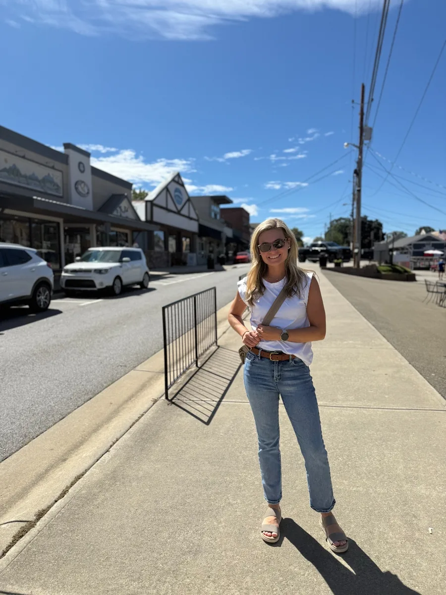 Chelsea standing on the sidewalk of Main Street in downtown Blue Ridge, Georgia, lined with storefronts under a deep blue sky